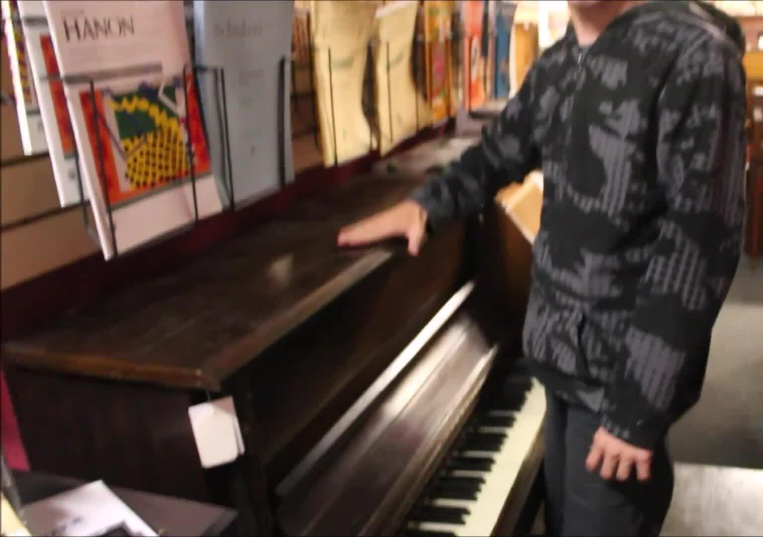 Close-up shot of the piano next to the presenter, highlighting its small size compared to the presenter's body.